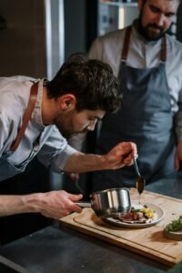 Two chefs in aprons skillfully plating a gourmet dish in an industrial kitchen setting.