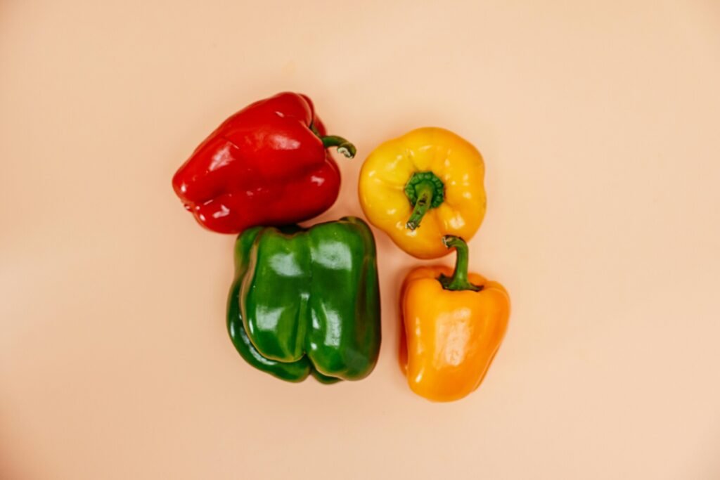 A vibrant display of red, green, yellow, and orange bell peppers arranged on a simple background.