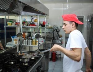 A young man working in a professional kitchen, cooking with a frying pan.