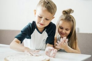 Two happy children enjoying baking, covered in flour while preparing dough at home.