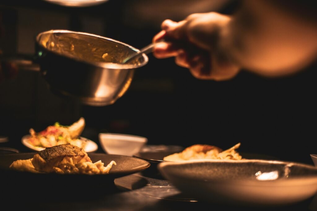 Gourmet dish being plated by a chef in a dimly lit restaurant's kitchen.